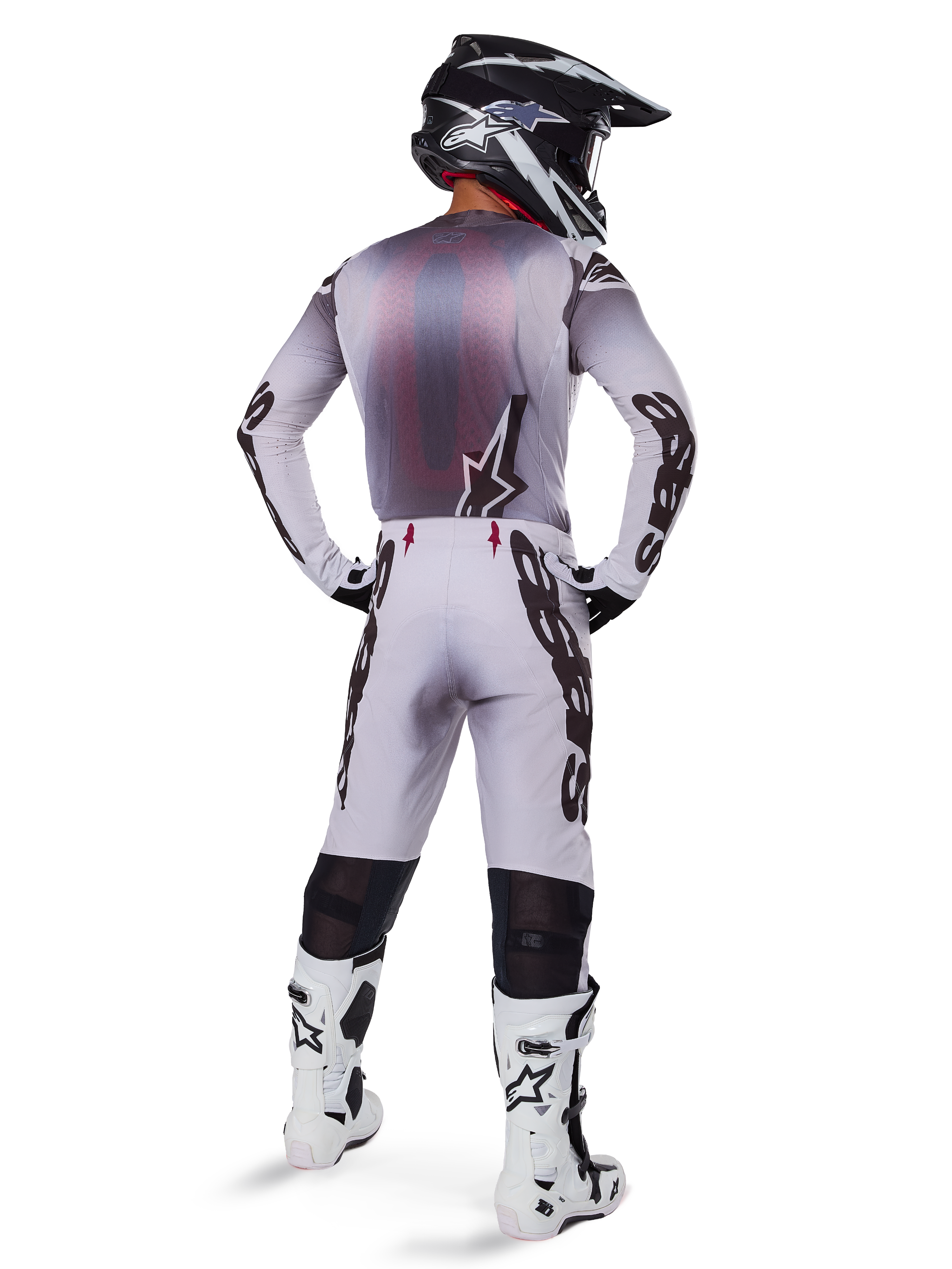 Motocrosskører set bagfra iført Alpinestars 2025 Supertech Maker bukser i sølv og sort, matchende langærmet jersey, sort og hvid hjelm og hvid-sorte støvler, med markant sort branding på benene, professionelt off-road racerudstyr
