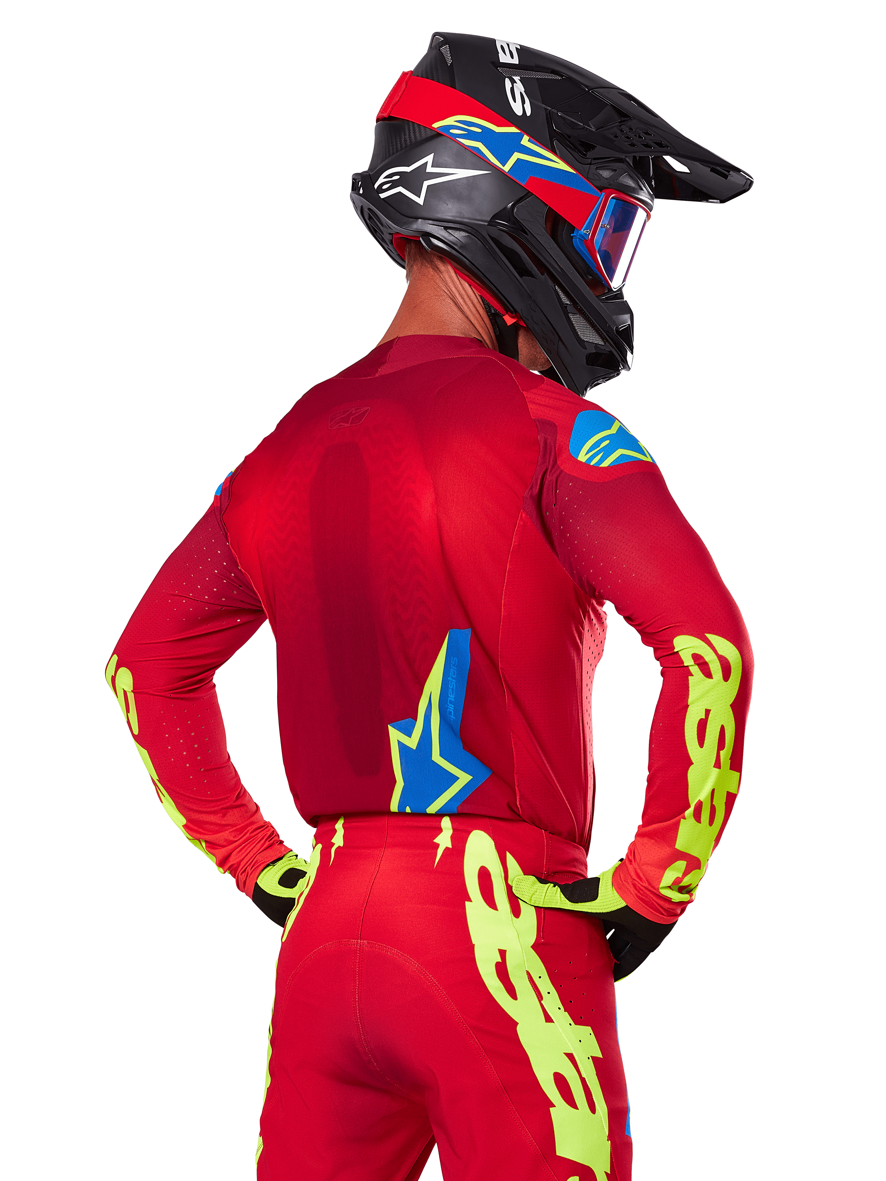 Bagfra af en motocrosskører iført Alpinestars 2025 Supertech Maker-udstyrssæt i rød, bestående af en rød jersey med neongul branding på ærmerne, matchende røde bukser, en sort hjelm med blå og røde detaljer samt koordinerende sorte og gule handsker.