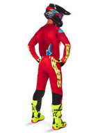 Motocross-kører set bagfra iført Alpinestars 2025 Supertech Maker-udstyrssæt, klar rød trøje med gul fluo-branding, matchende røde bukser med gule detaljer, sort hjelm med røde og blå detaljer, neongule støvler, koordineret professionelt raceroutfit til terrænkørsel