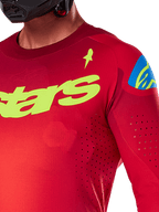 Alpinestars 2025 Supertech Maker trøje, motocross-trøje, rød og gul fluo, nærbillede med laserskårne perforeringer, gult Alpinestars-logo på brystet, blå skulderdetalje, åndbart strækmesh-materiale