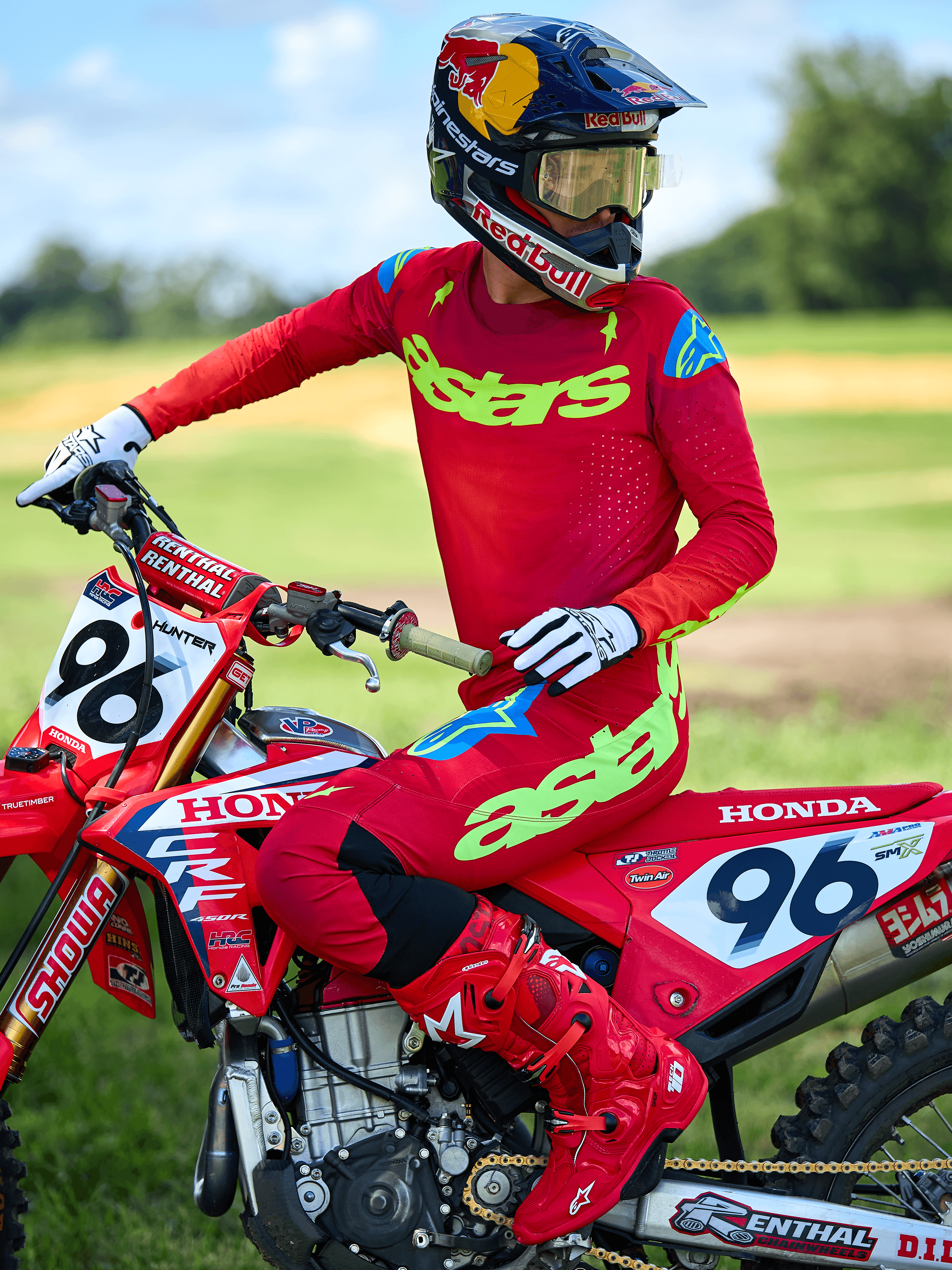 Motocross-kører iført Alpinestars 2025 Supertech Maker Jersey, klar rød med neongul 'astars'-branding, matchende røde bukser og støvler, hvide og sorte handsker, siddende på en rød Honda-racermaskine i udendørs omgivelser