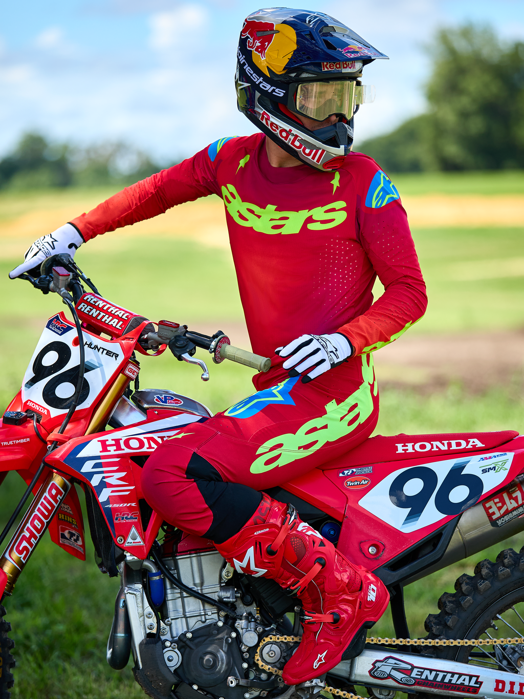 Motocrossrytter på en rød Honda-motorcykel iført Alpinestars 2025 Supertech Maker-udstyrssæt i rød, bestående af en rød trøje med neongrøn 'astars'-branding og blå skulderdetaljer, matchende røde bukser, helt røde støvler, hvide handsker og en Red Bull-hjelm, professionelt racersæt til terrænkørsel