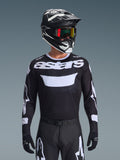 Alpinestars 2026 Racer Air Riway jersey, sort og hvid motocross-trøje med 'astars'-branding, båret af en kører med matchende sort hjelm, goggles og bukser, med åndbare mesh-paneler til off-road racing.