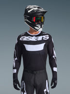 Alpinestars 2026 Racer Air Riway jersey, sort og hvid motocross-trøje med 'astars'-branding, båret af en kører med matchende sort hjelm, goggles og bukser, med åndbare mesh-paneler til off-road racing.