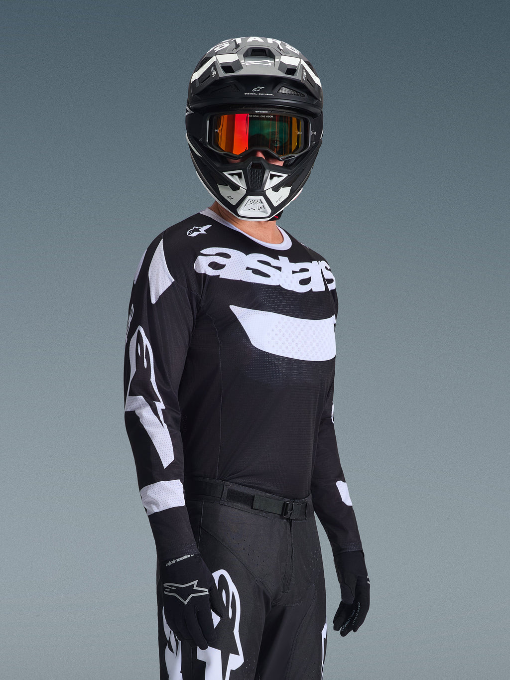 Motocrosskører iført 2026 Racer Air Riway Jersey, sort og hvid trøje med 'astars'-logo, matchende sort og hvid hjelm med orange spejlglas-goggles, sorte motocrossbukser og handsker, koordineret outfit til off-road racing