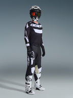Motocrosskører i komplet racerudstyr, 2026 Racer Air Riway-trøje i sort og hvid, matchende sorte bukser med store hvide Alpinestars-logoer, sort hjelm med hvide detaljer og orange goggles, hvide og sorte støvler, koordineret outfit til professionel off-road kørsel