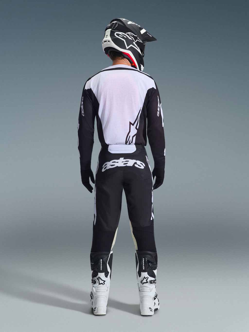 Alpinestars 2026 Racer Air Riway trøje i sort og hvid, set bagfra af motocrosskører, åndbart mesh-rygpanel, matchende sorte motocrossbukser med hvidt 'astars'-branding, sort og hvid hjelm og hvide racingstøvler.