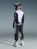 Motocrosskører set bagfra iført 2026 Racer Air Riway Jersey i sort og hvid, der fremviser det store hvide mesh-bagpanel for luftgennemstrømning, kombineret med sorte bukser, sort og hvid hjelm og hvide racerstøvler, komplet professionelt udstyr til off-road ydeevne.