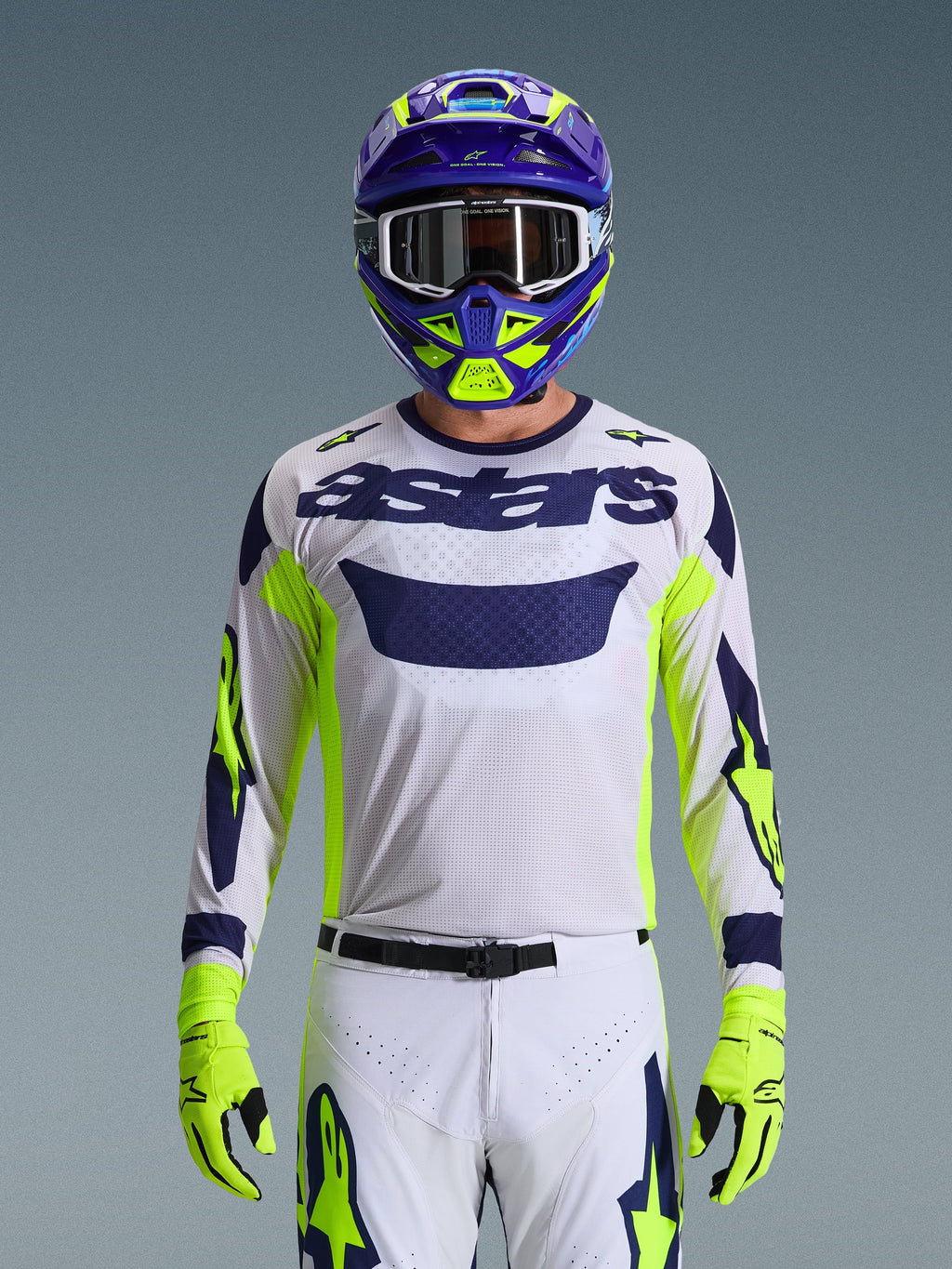 Alpinestars 2026 Racer Air Riway trøje, lysegrå med mørkeblåt astars-logo, neongule og blå detaljer på ærmerne, båret af en motocrosskører med matchende lilla og neongul hjelm og handsker, teknisk mesh-materiale til off-road racing