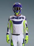 Alpinestars 2026 Racer Air Riway trøje, lysegrå med mørkeblåt astars-logo, neongule og blå detaljer på ærmerne, båret af en motocrosskører med matchende lilla og neongul hjelm og handsker, teknisk mesh-materiale til off-road racing