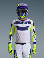 Alpinestars 2026 Racer Air Riway trøje, lysegrå med mørkeblåt astars-logo, neongule og blå detaljer på ærmerne, båret af en motocrosskører med matchende lilla og neongul hjelm og handsker, teknisk mesh-materiale til off-road racing