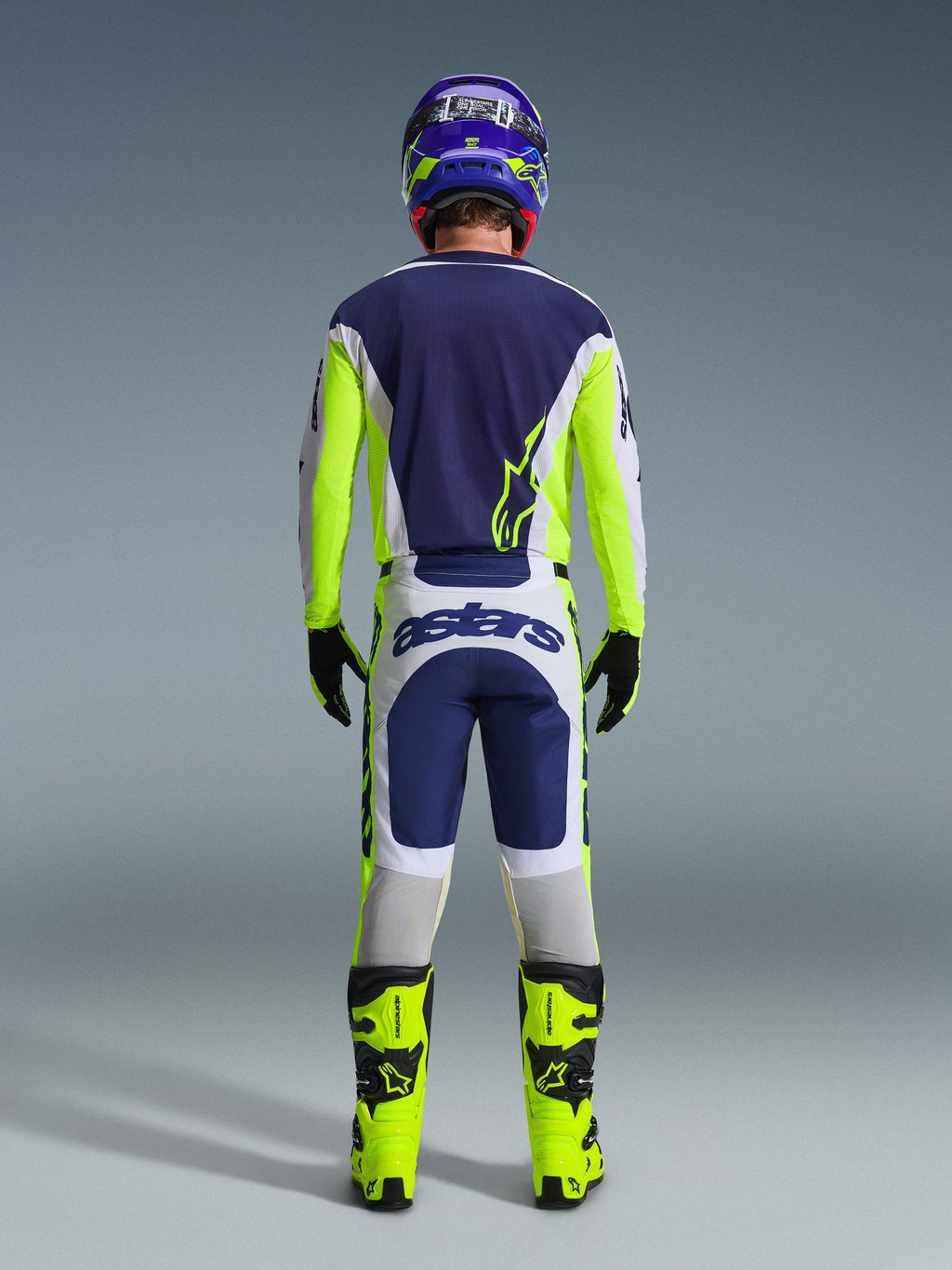 Bagsidevisning af en motocrosskører iført Alpinestars 2026 Racer Air Riway-trøje og matchende bukser i Light Gray Yellow Fluo Blue, kombineret med neongule støvler og en matchende hjelm, som viser et komplet off-road racersæt.