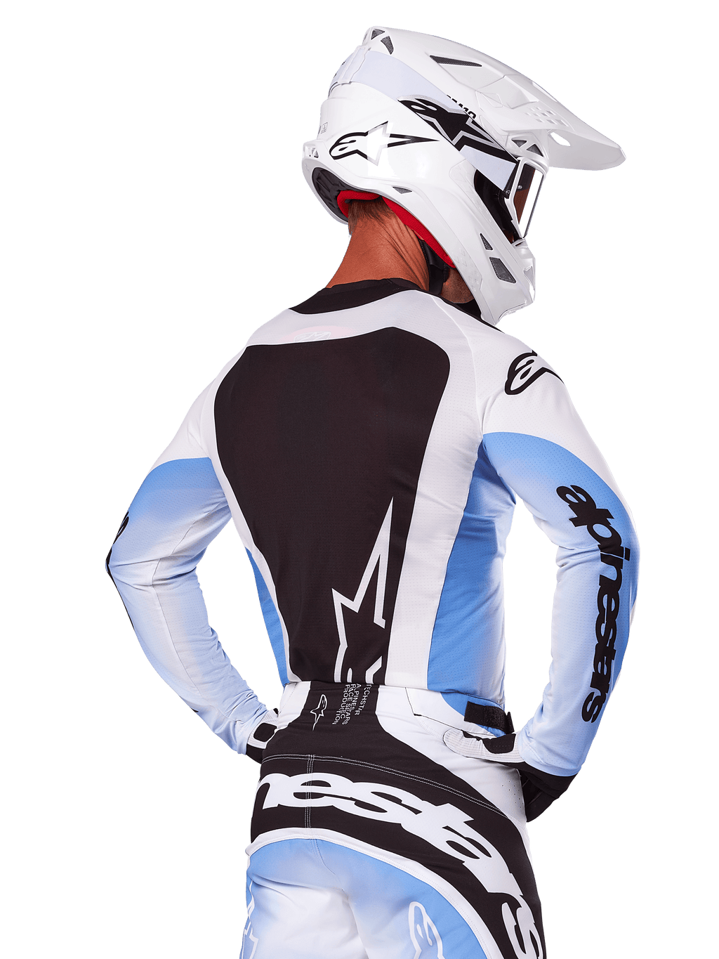 Motocrosskører set bagfra iført Alpinestars 2025 Techstar Melt-udstyrssæt i hvid og blå, jersey med et stort sort rygpanel med hvidt stjernelogo og lyseblå ærmer med graduering, matchende hvide og blå bukser, hvid racerhjelm og sort-hvide handsker, koordineret præstationsudstyr til motocross