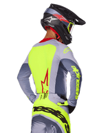 Alpinestars 2025 Techstar Melt Jersey, Bright Red Gray, back view of motocross rider wearing gray and neon yellow racing gear, red star logo on back, matching black and red helmet, performance off-road apparel