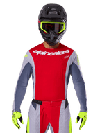 Motocross rider wearing 2025 Techstar Melt Jersey and matching pants, Bright Red and Gray with white Alpinestars branding, black helmet with neon yellow goggles, matching neon yellow gloves, ventilated performance gear for off-road racing