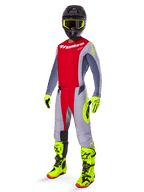 Motocross rider wearing Alpinestars 2025 Techstar Melt Jersey in Bright Red and Gray, featuring a red chest and gray sleeves with fluorescent yellow accents. Paired with matching pants, bright yellow racing boots and gloves, and a black helmet with yellow-framed goggles for a complete off-road racing kit.