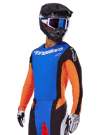 Alpinestars 2025 Techstar Melt udstyrssæt, motocrosskører iført blå jersey med orange ærmer og sorte sidepaneler, matchende blå og sorte bukser, sort hjelm med blå goggles, hvide og sorte handsker, atletisk race-fit motocrossbeklædning