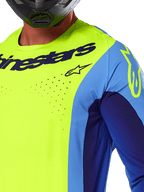 Alpinestars 2025 Techstar Melt trøje, motocross trøje, gul fluo og blå, med laserskårne perforeringer og markant logo på brystet, atletisk pasform til off-road racing, nærbillede med en sort hjelm