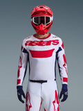 Motocrosskører iført Alpinestars 2026 Racer Riway-trøje i hvid, blå og rød, med et stort rødt 'astars'-logo på brystet, navyblå sidepaneler, matchende hvide og røde motocrossbukser, rød hjelm med hvide goggles og navyblå handsker, komplet off-road racingudstyrssæt.