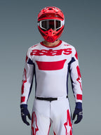 Motocrosskører iført Alpinestars 2026 Racer Riway-trøje i hvid, blå og rød, med et stort rødt 'astars'-logo på brystet, navyblå sidepaneler, matchende hvide og røde motocrossbukser, rød hjelm med hvide goggles og navyblå handsker, komplet off-road racingudstyrssæt.