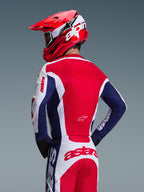 Motocrosskører set bagfra iført Alpinestars 2026 Racer Riway-trøje, hvid, blå og rød farvekombination, matchende off-road-bukser med tydelig astars-branding, rød hjelm med hvidt Alpinestars-logo, sorte handsker, koordineret motocross-racerudstyr
