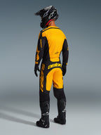 Motocrosskører set bagfra iført Alpinestars 2026 Racer Riway-udstyrssæt, gul og sort trøje og matchende bukser, sort hjelm, sorte handsker og sorte støvler med hvide detaljer, koordineret outfit til professionel terrænkørsel.