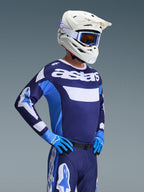 Motocrosskører iført Alpinestars 2026 Racer Riway-trøje i UCLA Blue White, med 'astars'-branding på brystet, kombineret med matchende blå motocrossbukser, hvid hjelm med goggles og blå handsker, højtydende off-road racingudstyr