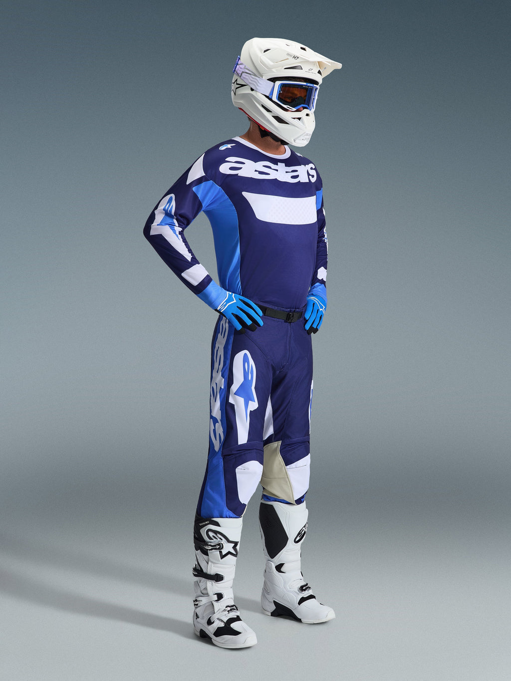 Motocrosskører iført Alpinestars 2026 Racer Riway-udstyrssæt i UCLA Blue og hvid, bestående af en blå og hvid trøje med 'astars'-branding, matchende bukser, en hvid hjelm med blå goggles og hvide off-road støvler, komplet raceroutfit til motocross.