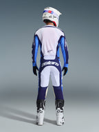 Set bagfra af en motocrosskører iført Alpinestars 2026 Racer Riway Jersey og bukser i Ucla Blue og hvid, koordineret med en hvid hjelm, sorte handsker og hvide motocrossstøvler, højpræstationsudstyr til off-road racing