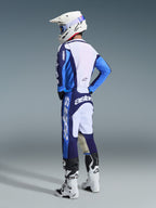 Motocross-kører iført 2026 Racer Riway Jersey i Ucla Blue og hvid, kombineret med matchende blå og hvide motocrossbukser, en hvid hjelm og hvide støvler, vist fra en trekvart vinkel bagfra for et komplet off-road racing-look.
