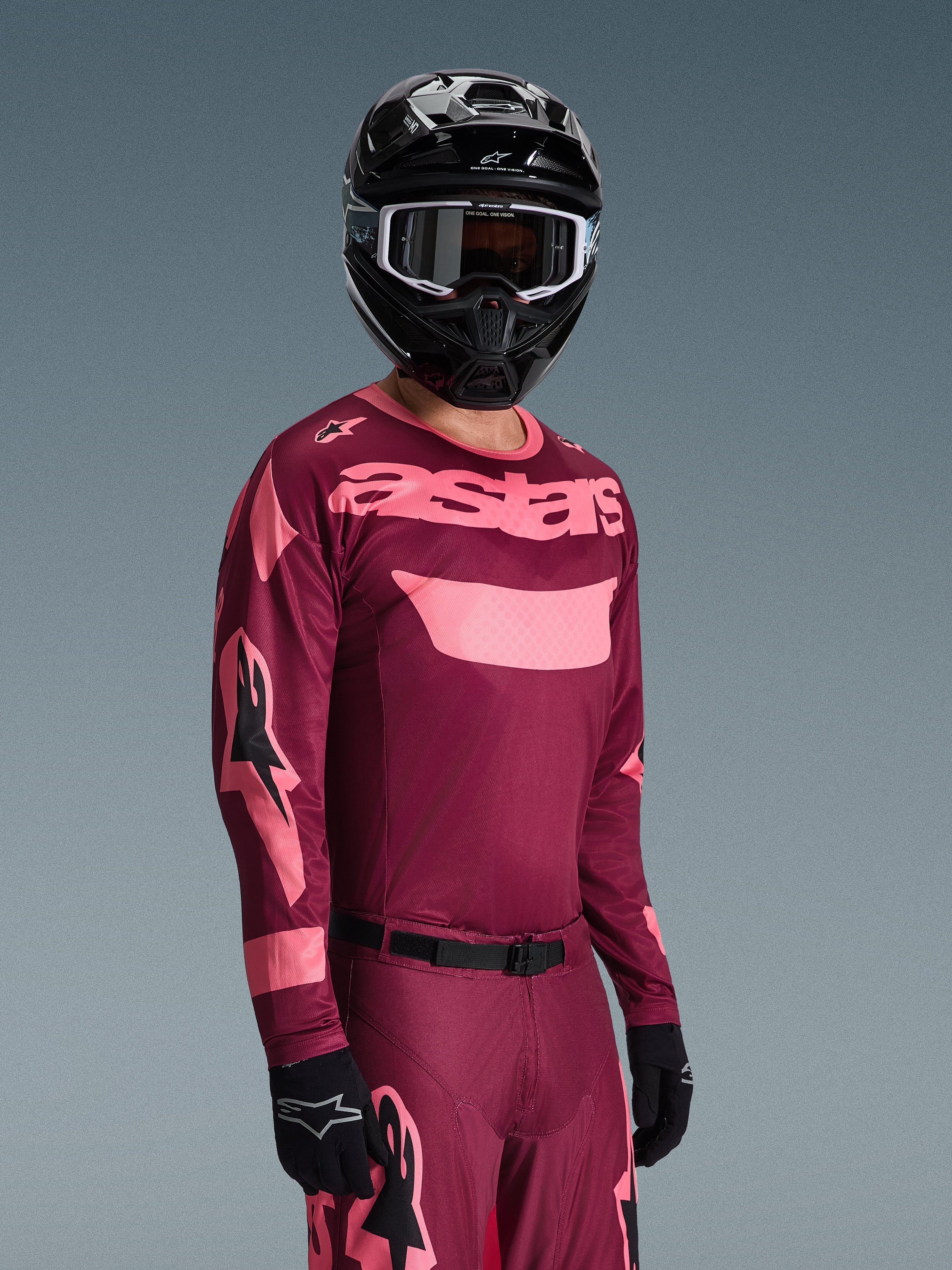 Motocross-kører iført Alpinestars 2026 Racer Riway Jersey i Dark Red Coral med matchende bukser, med koralfarvet 'astars'-branding på brystet, kombineret med en sort hjelm og sorte handsker, koordineret sæt til off-road racing.