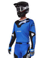 Alpinestars 2025 Racer Veil-udstyrssæt, blå motocross-jersey med sort og hvid grafik, båret med matchende bukser, sort hjelm, hvide goggles og blå handsker, teknisk beklædning til off-road racing