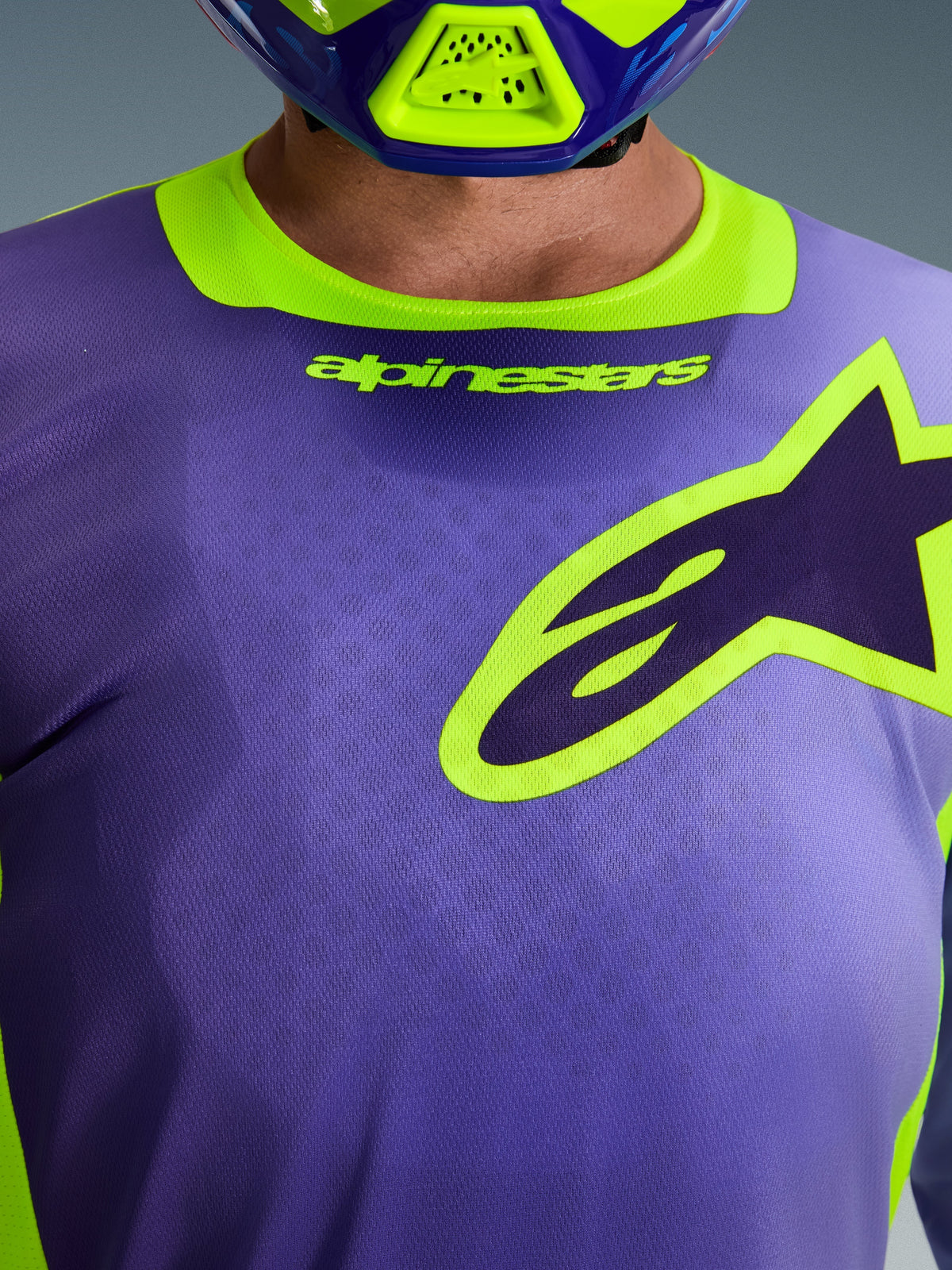 Alpinestars 2026 Racer Portl-trøje, motocross-trøje, lilla og neongul, nærbillede af brystområdet med et stort Alpinestars-logo med gul kant, strækhalskrave med branding, teknisk fugttransporterende polyfabric