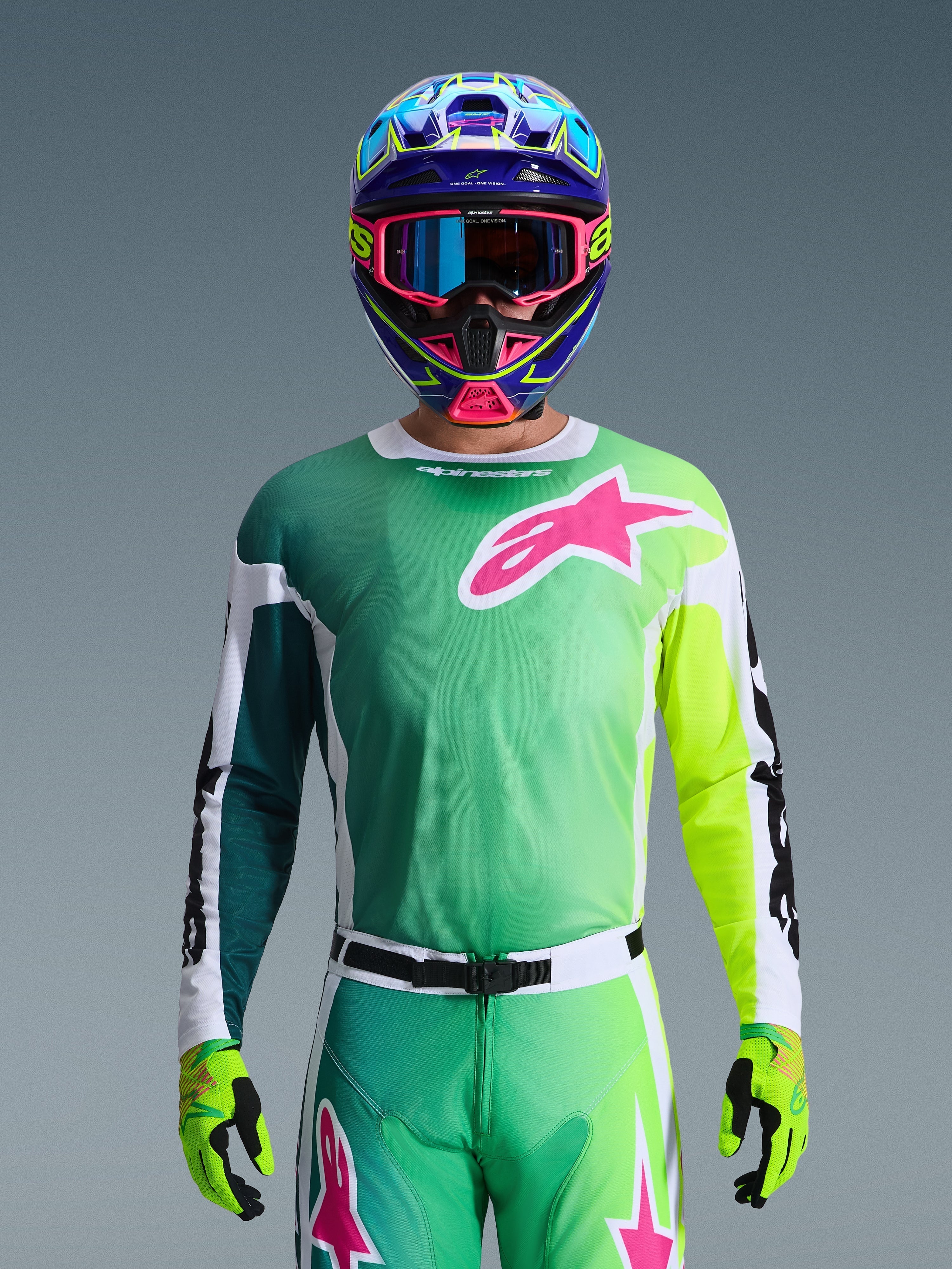 Alpinestars 2026 Racer Portl trøje, motocross-trøje, grøn, hvid og sort med et stort pink Alpinestars-logo på brystet, båret af en kører med en farvestrålende flerfarvet hjelm og matchende briller, professionelt off-road racerudstyr