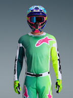 Alpinestars 2026 Racer Portl Gear Sæt, motocross-kører iført grøn og gul gradient-jersey med lyserødt Astars-logo, matchende bukser, farverig blå og lyserød hjelm med blå goggles og limegrønne handsker, koordineret professionelt off-road racing-outfit