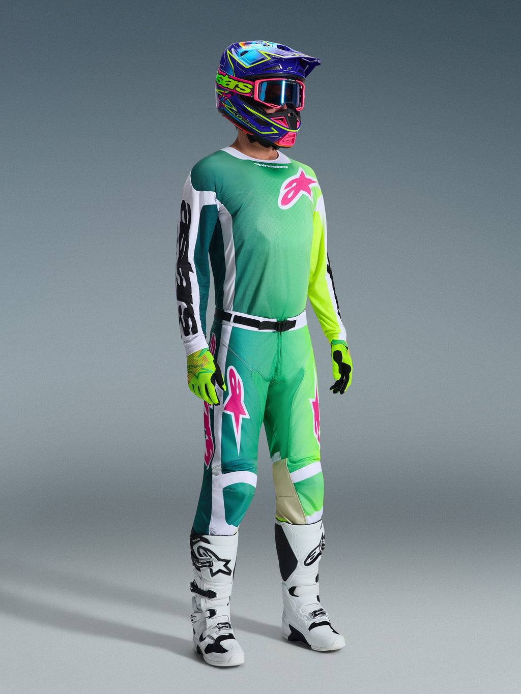 Motocross-kører iført komplet racerudstyr, 2026 Racer Portl-trøje i grøn med hvide og sorte ærmer og pink logo, matchende grønne bukser med pink detaljer, flerfarvet hjelm med crossbriller, hvide og sorte støvler og grønne handsker, koordineret sæt til terrænkørsel