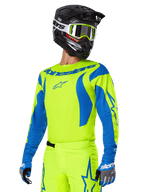 Alpinestars 2025 Fluid Haul-udstyrssæt, motocross-trøje og -bukser, klar gul og blå, båret med en sort hjelm og briller med gul ramme, har bølgeagtige blå mønstre på ærmerne og blå stjernelogoer på bukserne, koordineret off-road racing-outfit