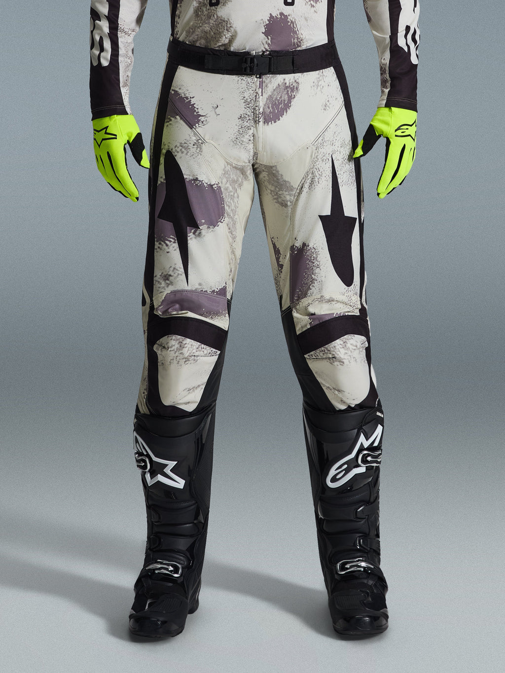 Alpinestars 2026 Racer Lahnd bukser, motocross-bukser, Sand Camo-mønster med grå og lilla abstrakt grafik, båret med neongule handsker og sorte støvler, med sorte stjernelogoer på lårene og et sort taljebælte, slidstærkt off-road racingudstyr