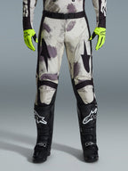 Alpinestars 2026 Racer Lahnd bukser, motocross-bukser, Sand Camo-mønster med grå og lilla abstrakt grafik, båret med neongule handsker og sorte støvler, med sorte stjernelogoer på lårene og et sort taljebælte, slidstærkt off-road racingudstyr