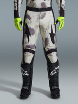Alpinestars 2026 Racer Lahnd Pants, Motocross Pants, Sand Camo pattern with gray and purple abstract graphics, worn with neon yellow gloves and black boots, featuring black star logos on the thighs and a black waist belt, durable off-road racing gear