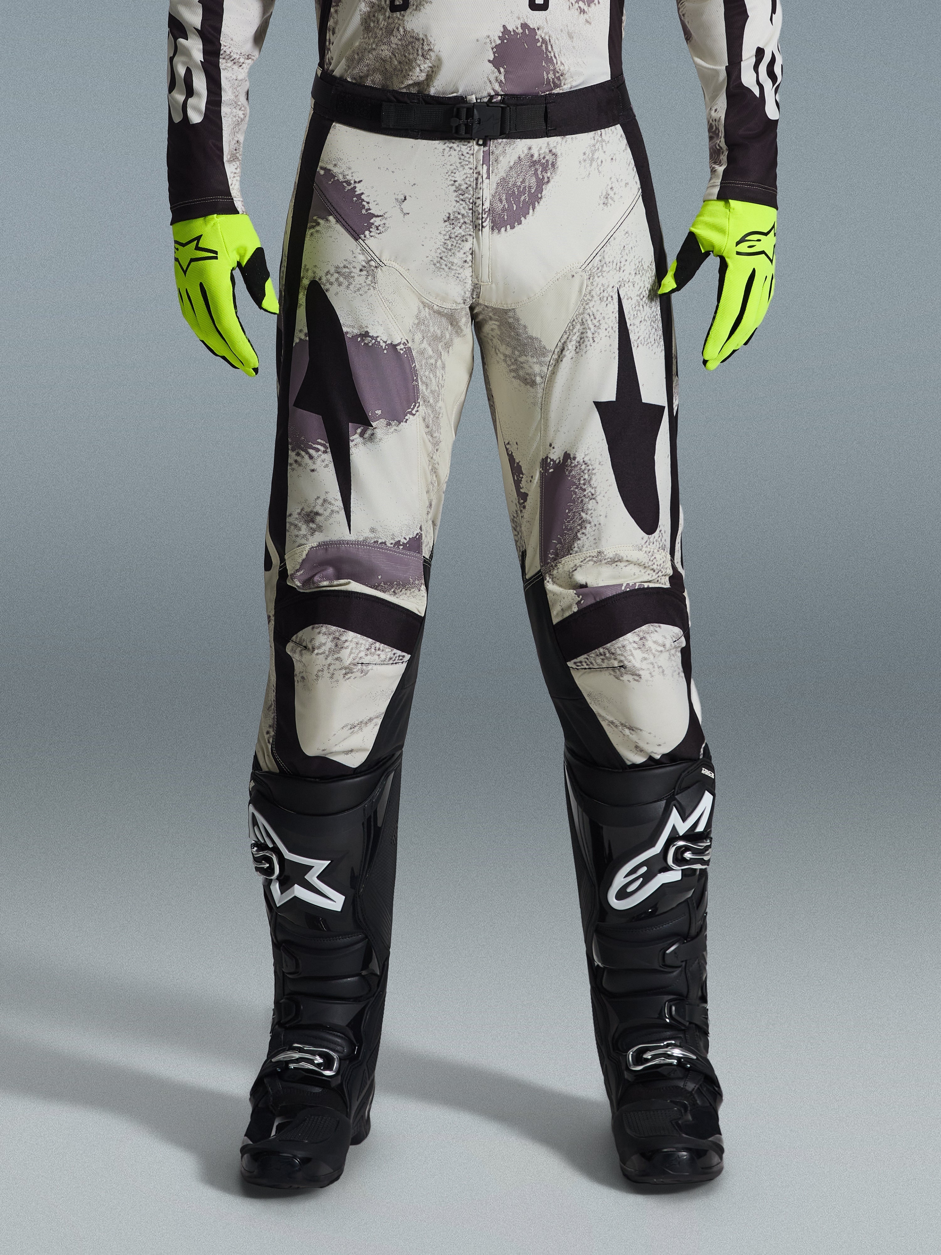 Alpinestars 2026 Racer Lahnd bukser, motocross-bukser, Sand Camo-mønster med grå og lilla abstrakt grafik, båret med neongule handsker og sorte støvler, med sorte stjernelogoer på lårene og et sort taljebælte, slidstærkt off-road racingudstyr