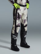 Alpinestars 2026 Racer Lahnd bukser, motocrossbukser, Sand Camo, båret med neongule handsker og sorte motocross-støvler, med abstrakt camouflage-mønster og sorte sidepaneler, ergonomisk off-road-design