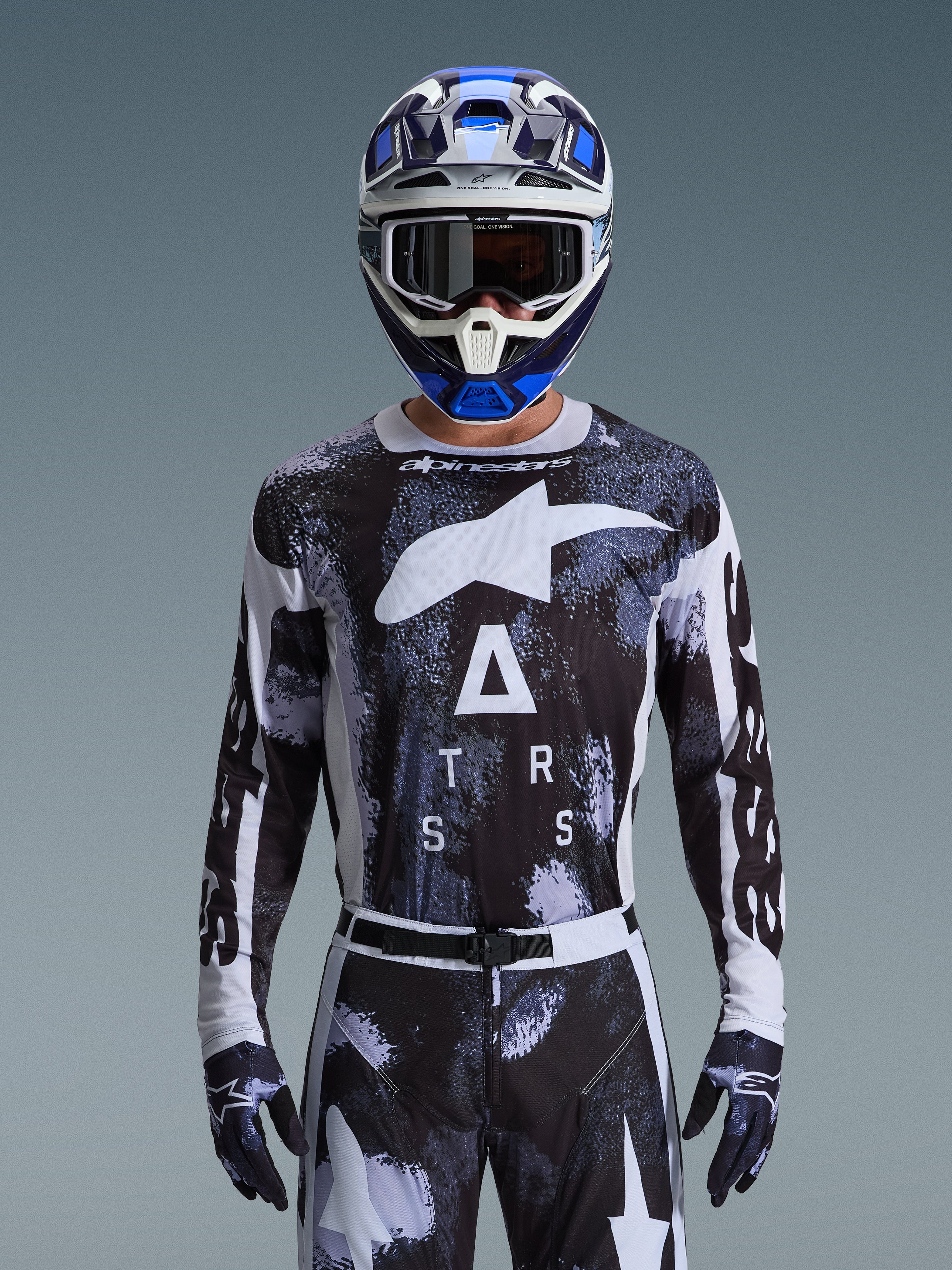 Motocrosskører iført Alpinestars 2026 Racer Lahnd-udstyrssæt, sort og hvid trøje med abstrakt camouflagemønster, store hvide logoer og "ATRS"-skrift, matchende bukser og handsker, blå og hvid hjelm med goggles, højtydende racerdragt til off-road motocross