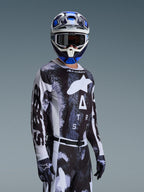 Motocross-kører iført Alpinestars 2026 Racer Lahnd-udstyrssæt, sort og hvid jersey med marmoreret blå og grå grafik, matchende bukser og handsker, blå og hvid hjelm med goggles, højtydende udstyr til terrænkørsel
