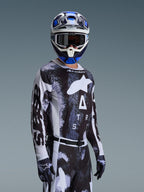 Motocrosskører iført Alpinestars 2026 Racer Lahnd Jersey i Iron Camo, med et sort og gråt camouflage-mønster og et stort hvidt Alpinestars-logo på brystet, stylet med matchende hjelm og handsker til off-road racing.