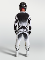 Alpinestars Techstar Swan trøje og gear-sæt, hvidt og sort motocrossudstyr til mænd med splatter-grafik, set bagfra med hjelm og hvide støvler.