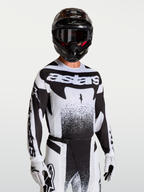 Alpinestars Techstar Swan trøje, herre-motocrosstrøje til terrænkørsel, sort og hvid, atletisk pasform med laserskåret ventilation, vist på model med hjelm og handsker.