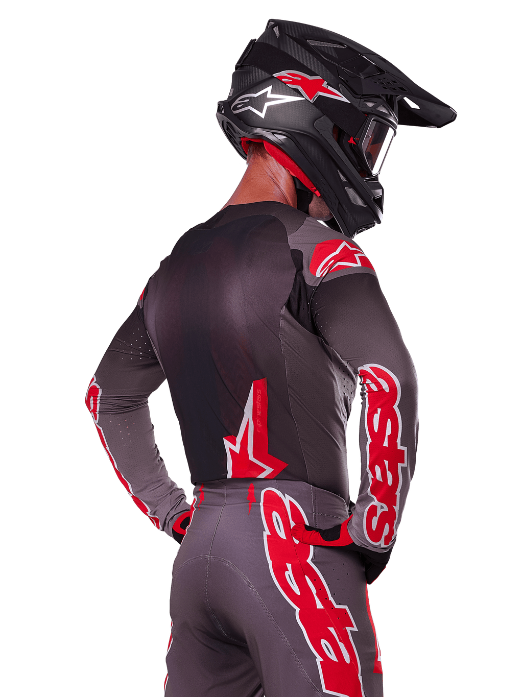 Alpinestars 2025 Supertech Lipan udstyrssæt, motocross-kører set bagfra, koksgrå jersey og bukser med markant rød 'astars'-branding på ærmerne og ryggen, kombineret med en sort hjelm