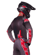 Alpinestars 2025 Supertech Lipan udstyrssæt, motocross-kører set bagfra, koksgrå jersey og bukser med markant rød 'astars'-branding på ærmerne og ryggen, kombineret med en sort hjelm