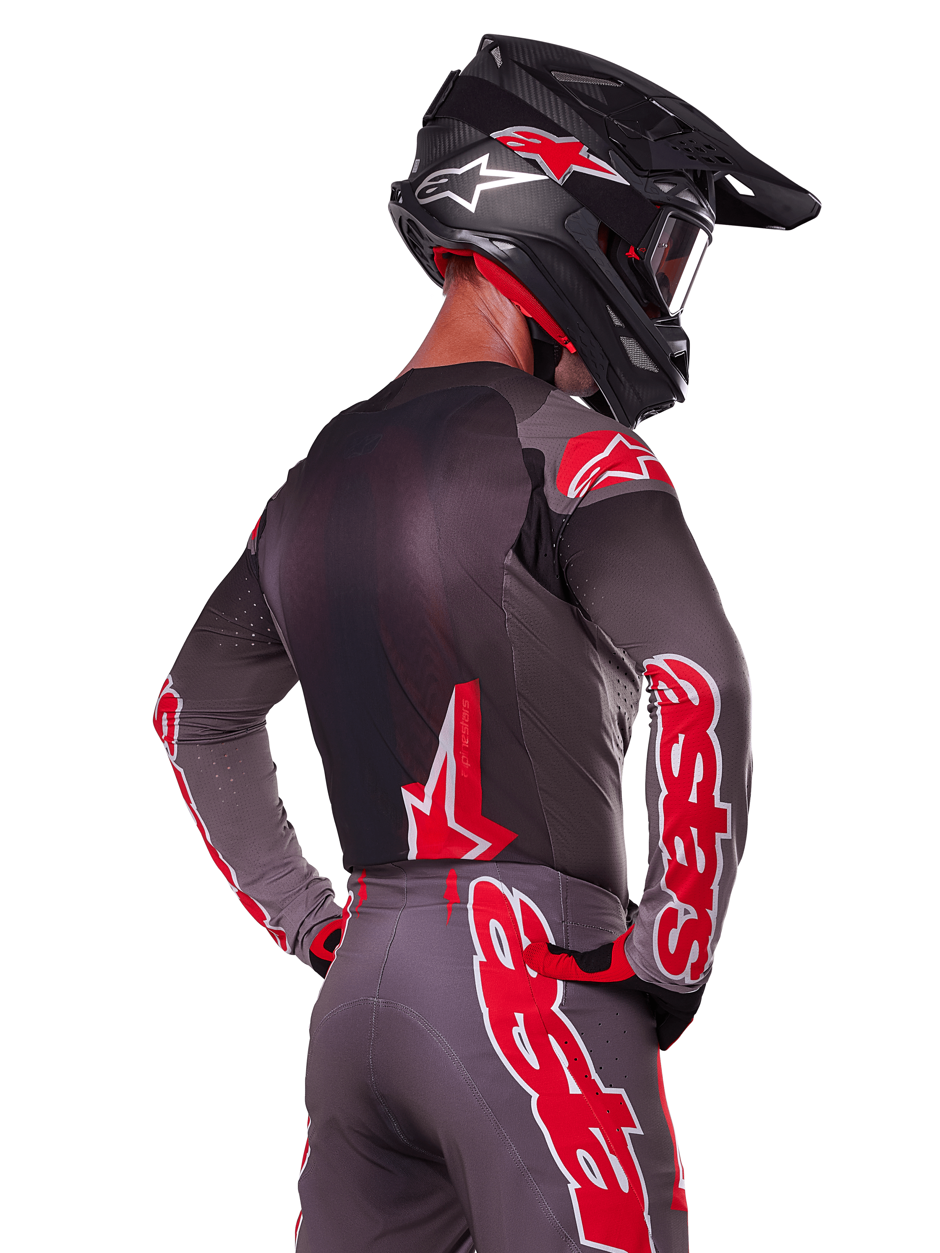 Alpinestars 2025 Supertech Lipan udstyrssæt, motocross-kører set bagfra, koksgrå jersey og bukser med markant rød 'astars'-branding på ærmerne og ryggen, kombineret med en sort hjelm